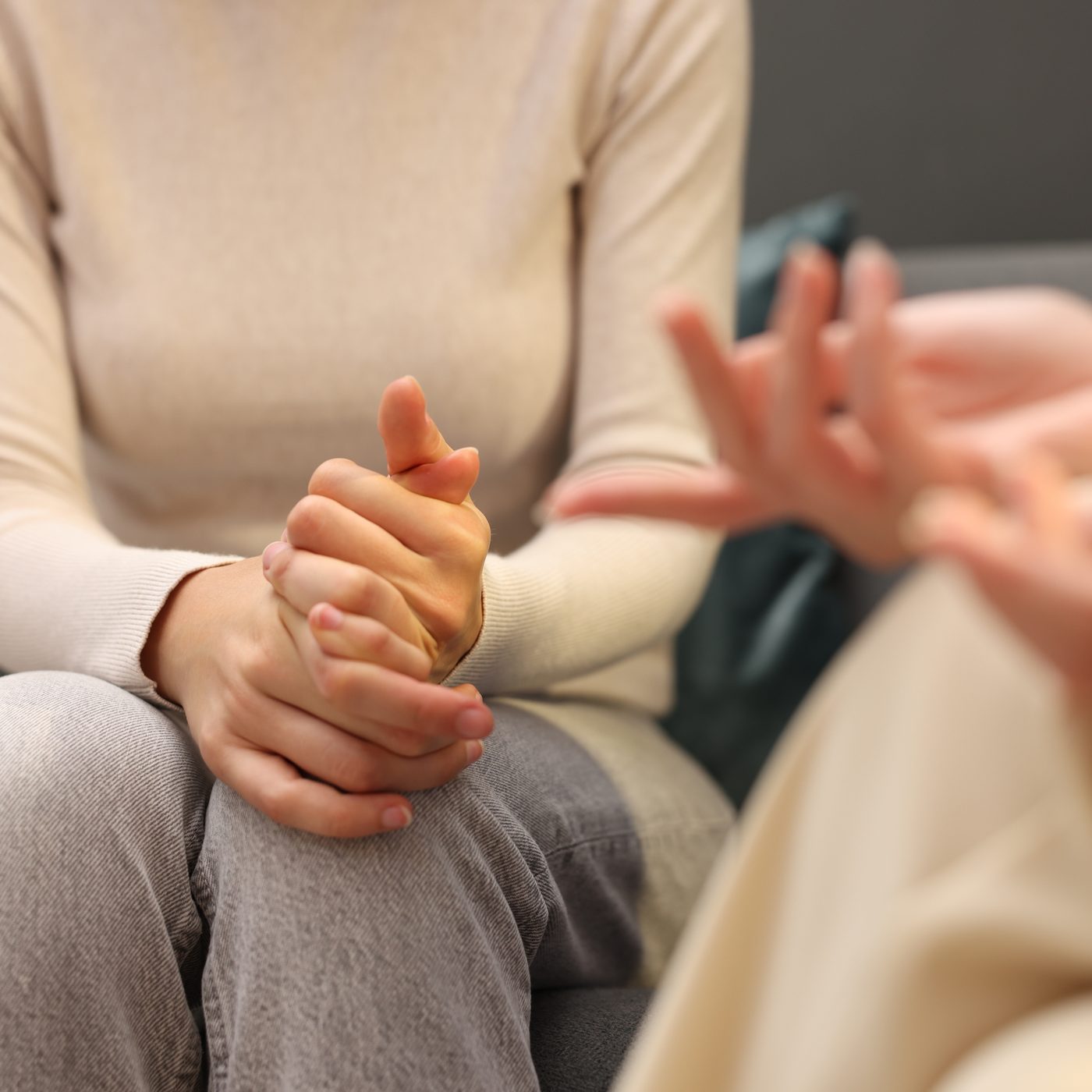 Duas pessoas sentadas conversando, uma com as mãos entrelaçadas no colo e a outra gesticulando